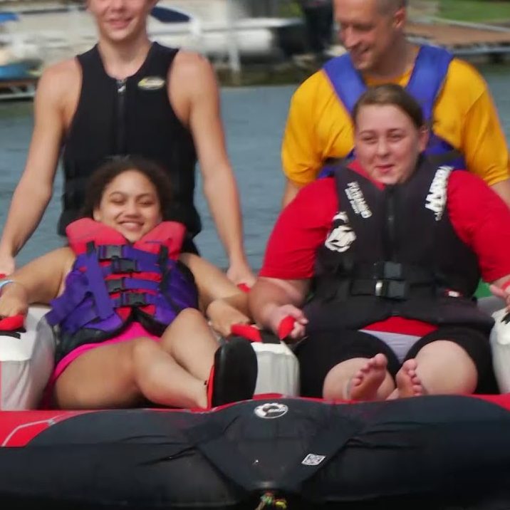 2 female tube riders with 2 volunteers behind them tubing around the lake