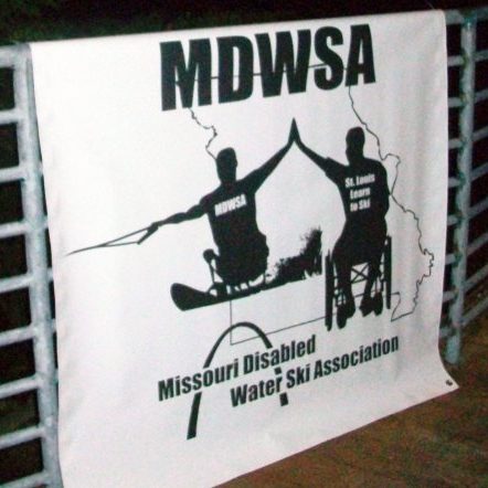 a black and white MDWSA banner that depicts an adult male skier in a sit ski giving a high five to a man in a wheelchair