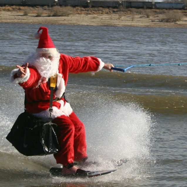 an adult male skier, dressed in a Santa suit with a very big black shoulder bag, is skiing the Mississippi River
