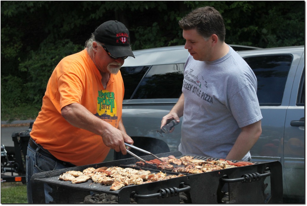 2 adult male volunteers are chatting and grilling chicken and hot dogs for lunch