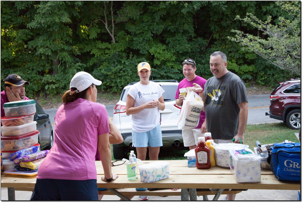 6 volunteers are standing around a picnic table discussing what to do when setting up for lunch