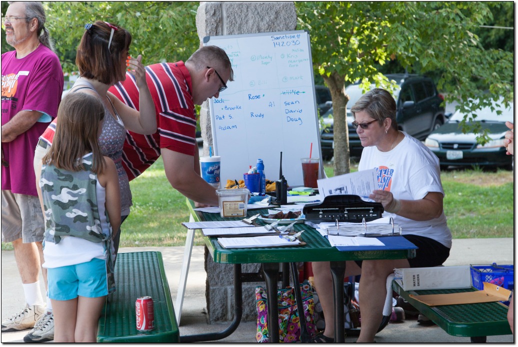 an adult female sitting at a picnic table (registration table) helping volunteers sign their waivers