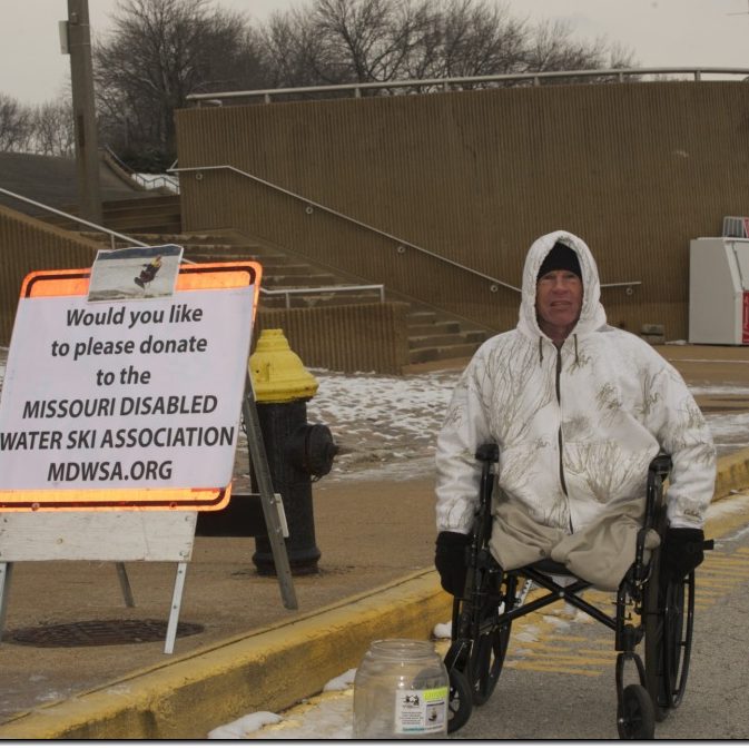 disabled adult male skier, sitting in a wheelchair and bundled up from the cold, at the St Louis RIverfront collecting donations for the Polar Bear Plunge