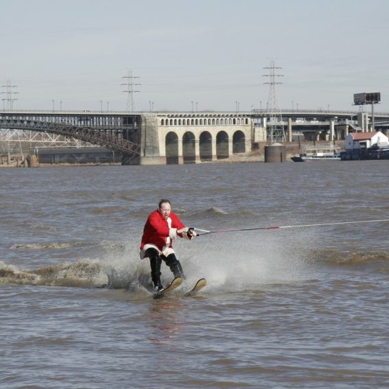 an adult male skier, dressed up like Santa, skiing on the Mississippi River