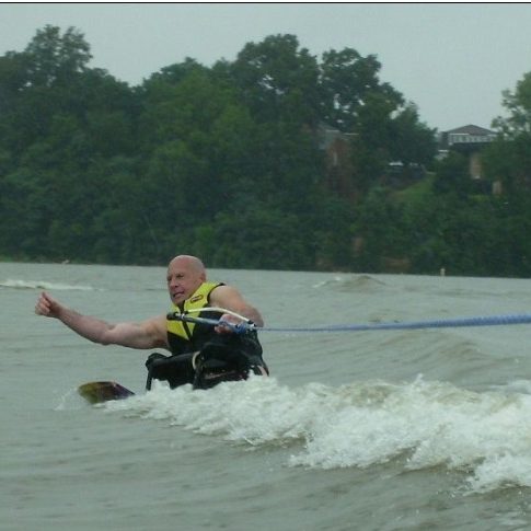 an adult male disabled sit skier jumping the wake with a very determined look on his face