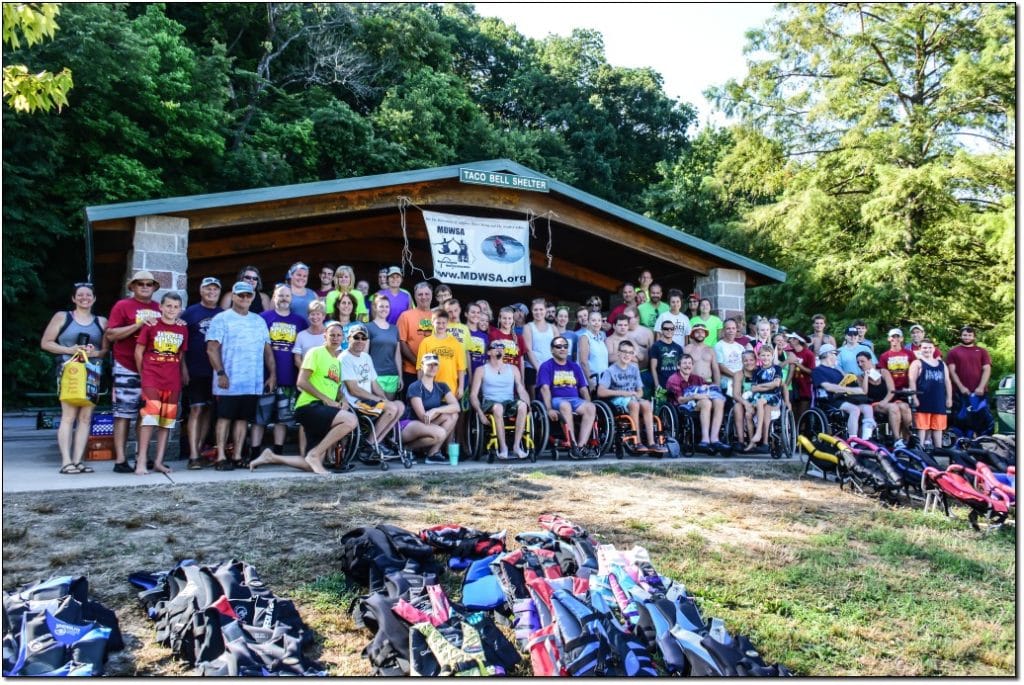 group photo, taken at the pavillion, of about 50 skiers and volunteers. The MDWSA banner is hanging from the rafters and there is ski equipment and life jackets on the ground in front of the group